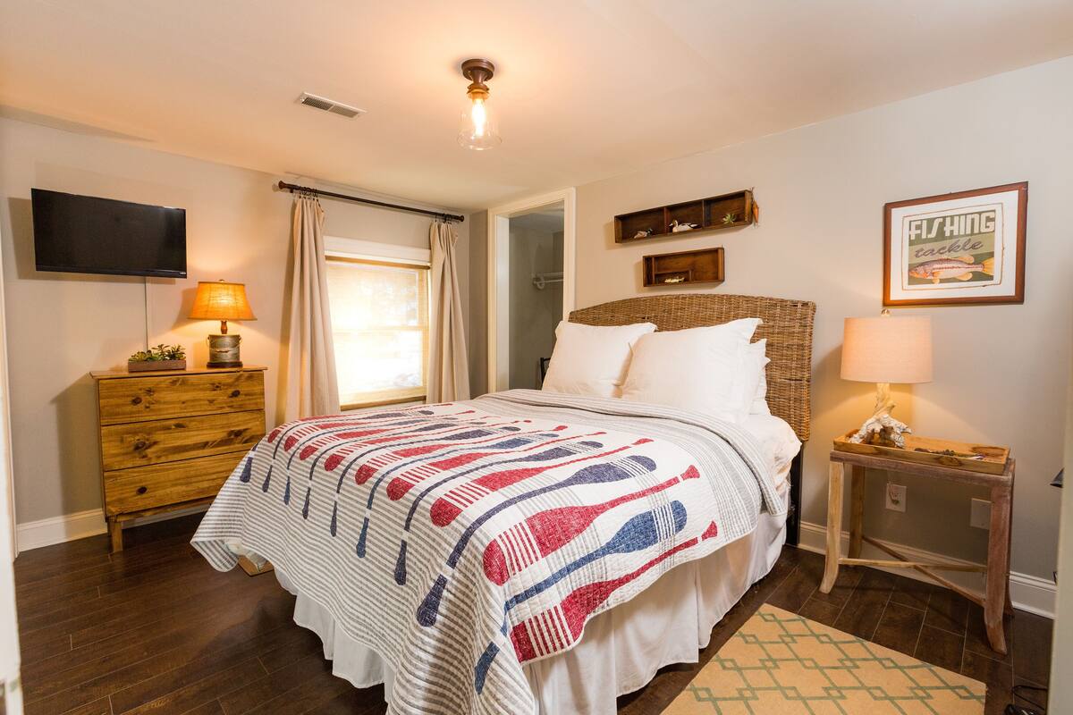 A bedroom with a bed, a dresser, a television, a lamp, and a framed picture on the wall.