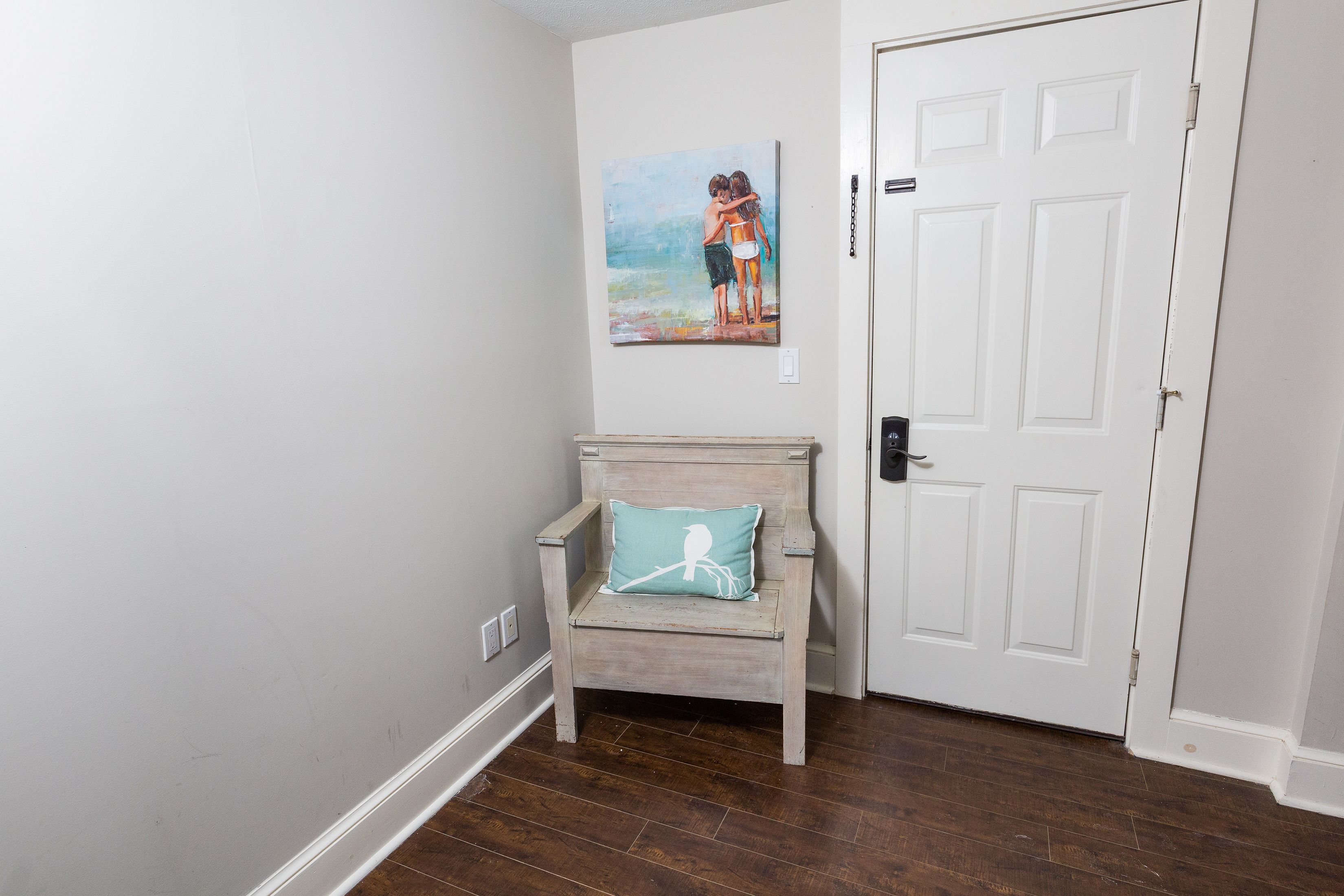 Un couloir avec une chaise en bois, un tableau accroché au mur et une porte blanche.