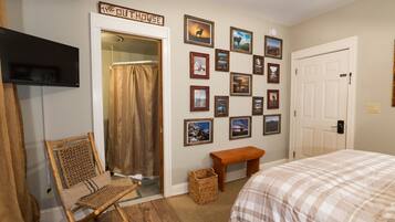 A bedroom with a bed, a chair, a bench, a wall with framed pictures, a door, and a television.