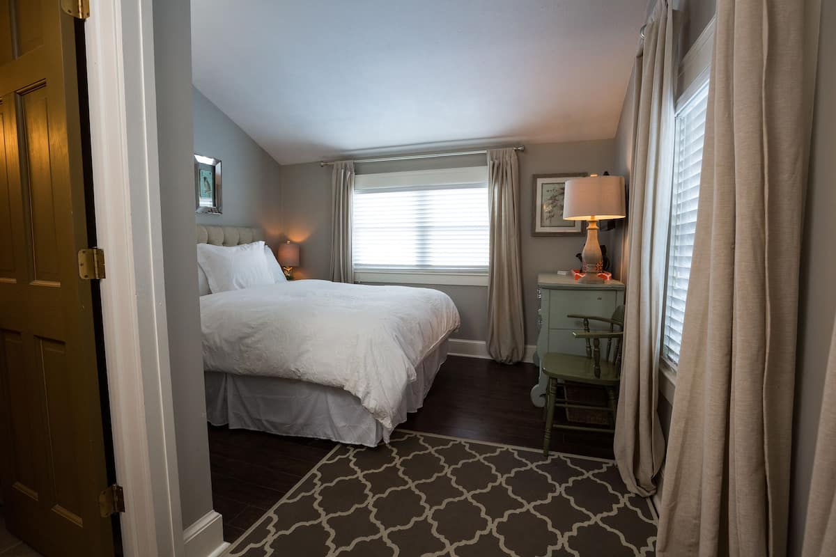 A hotel room with a large bed, a desk with a chair, a window with curtains, and a lamp.