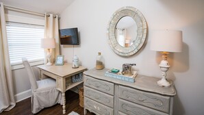 Un dormitorio con escritorio, una silla, televisor, cómoda y espejo.