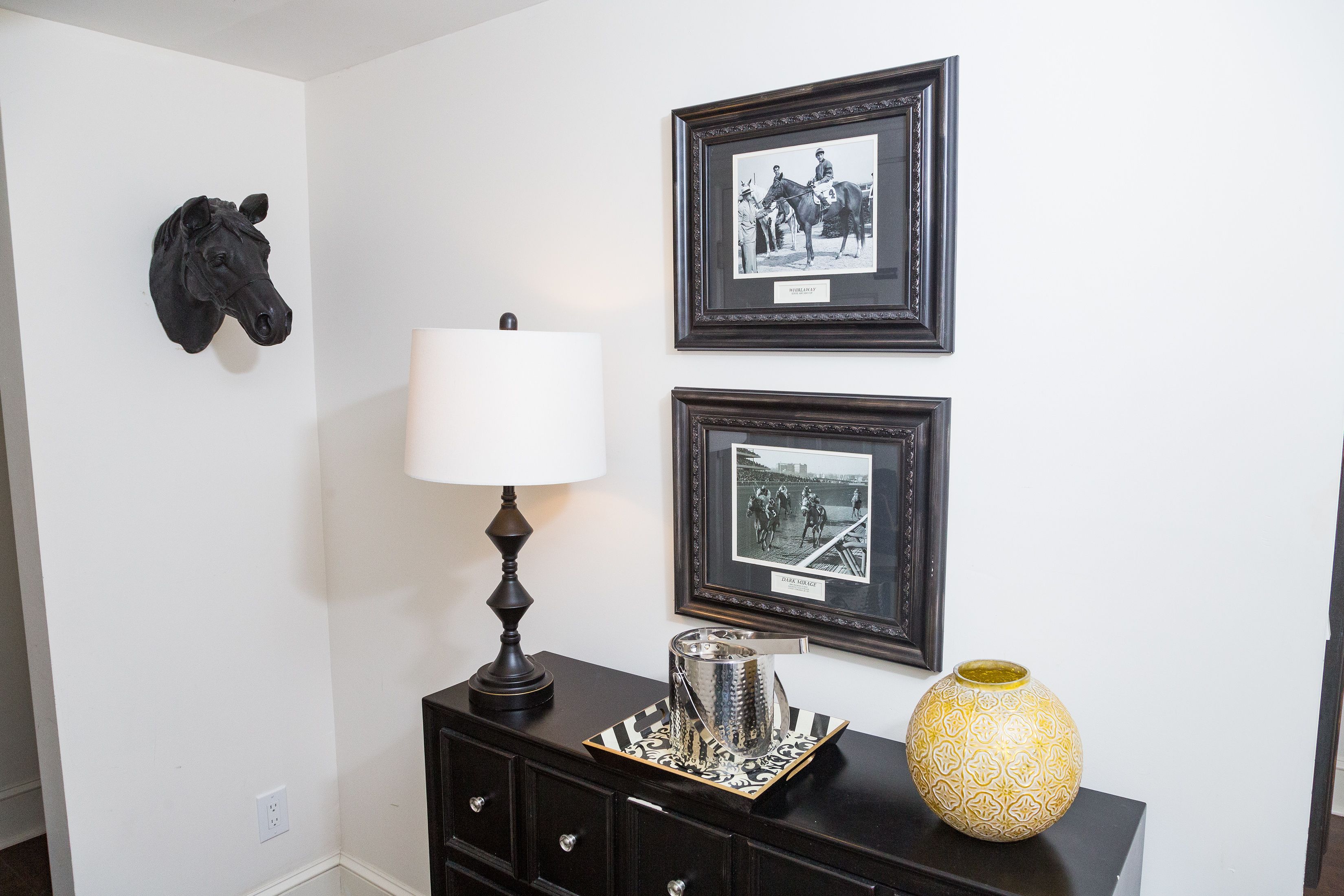 A room with a black horse head decoration, a lamp, and two framed photographs on the wall.
