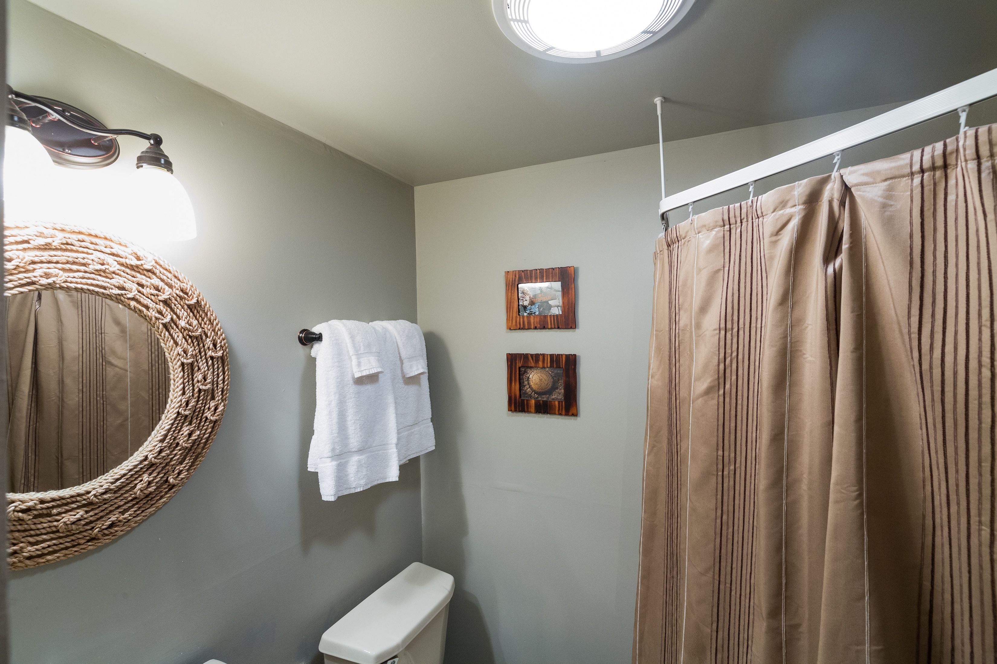 Un baño con inodoro, toallero con toallas, espejo y cortina de ducha.