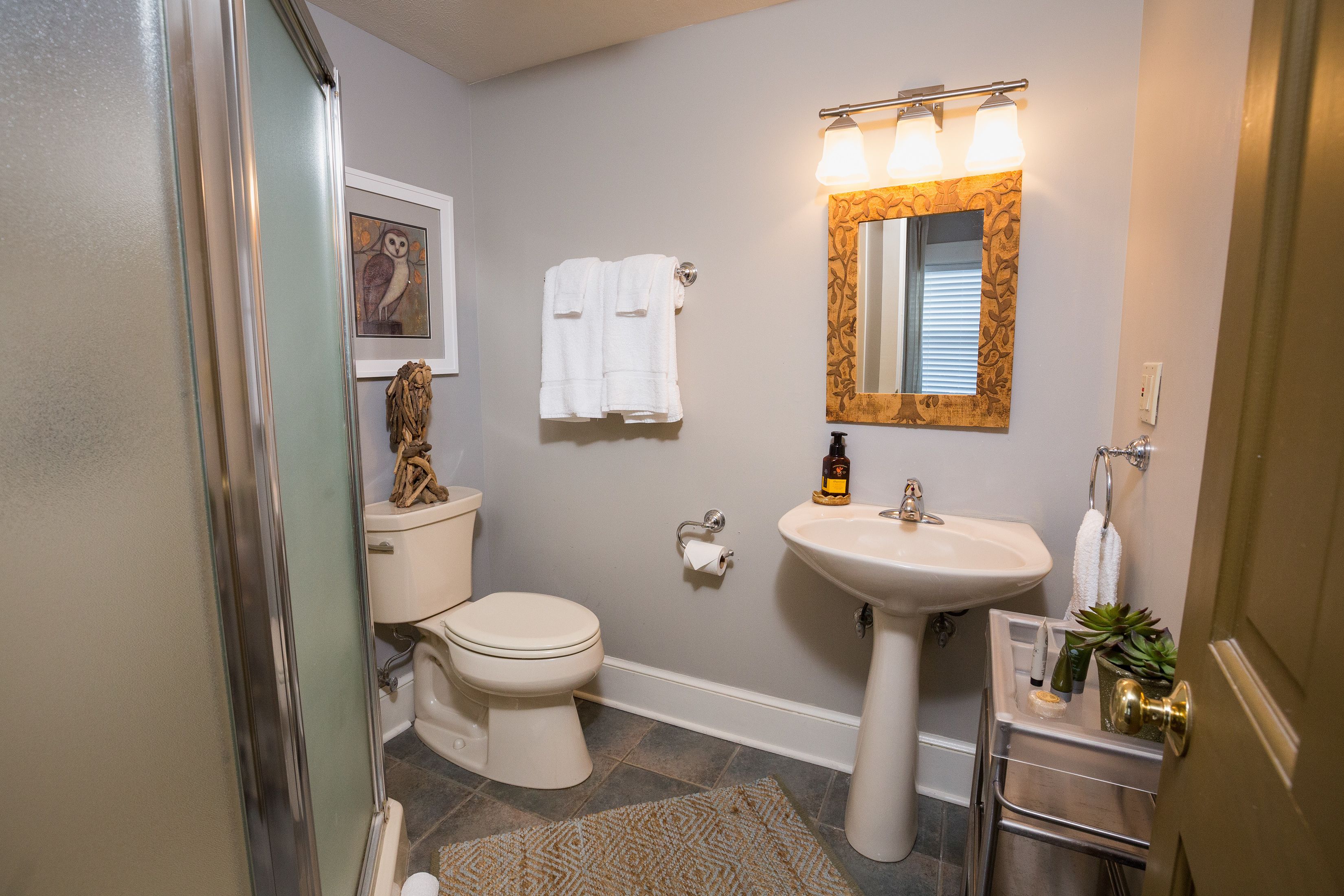 A bathroom with a toilet, sink, and mirror. There are towels hanging on the wall and a rug on the floor.