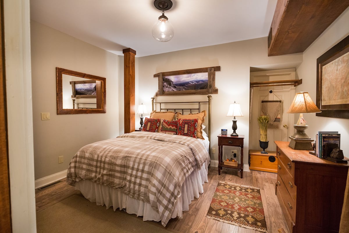 A bedroom with a bed, bedside lamps, a dresser, a mirror, and a painting on the wall.