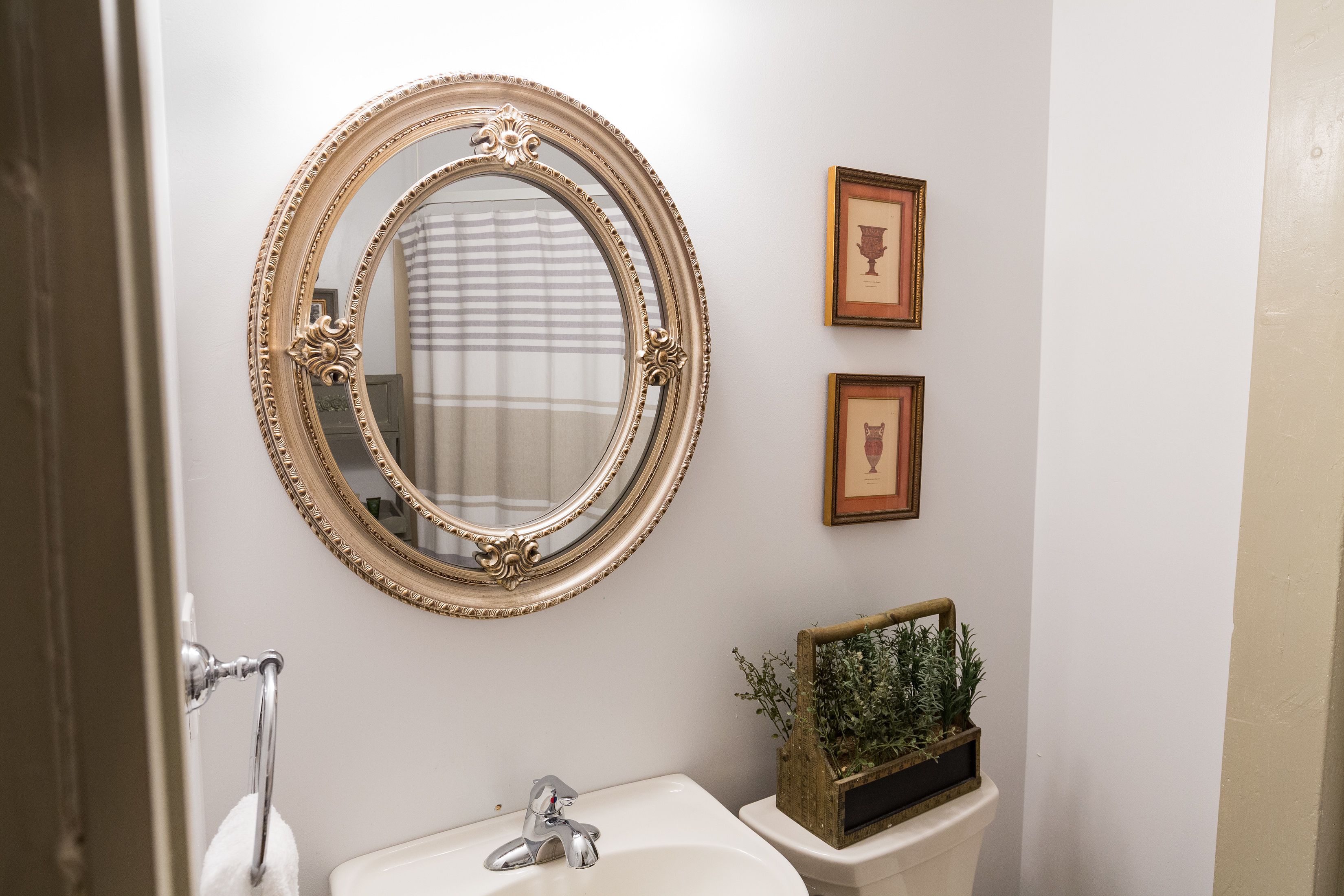 A bathroom with a round mirror, a sink, and two framed pictures on the wall.