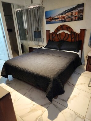 A bedroom with a bed, a nightstand, a lamp, a painting, and a door. - Hotel Riparbella (Santo Domingo)