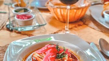 Una mesa de comedor con un plato de comida, un vaso de bebida roja y recipientes pequeños de condimentos.