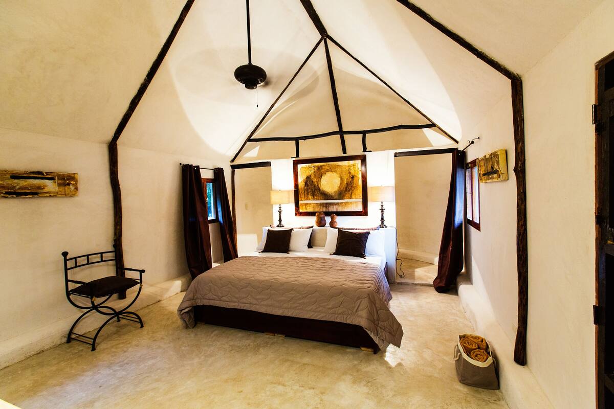 A bedroom with a large bed, a chair, and a painting on the wall.