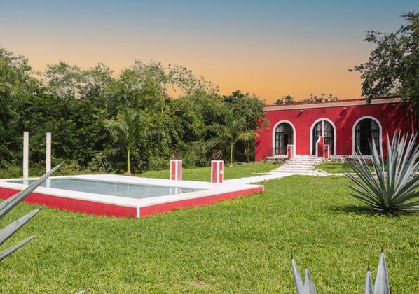 Un bâtiment rouge doté de fenêtres en arc de cercle, d’une piscine rectangulaire et d’une pelouse bien entretenue.