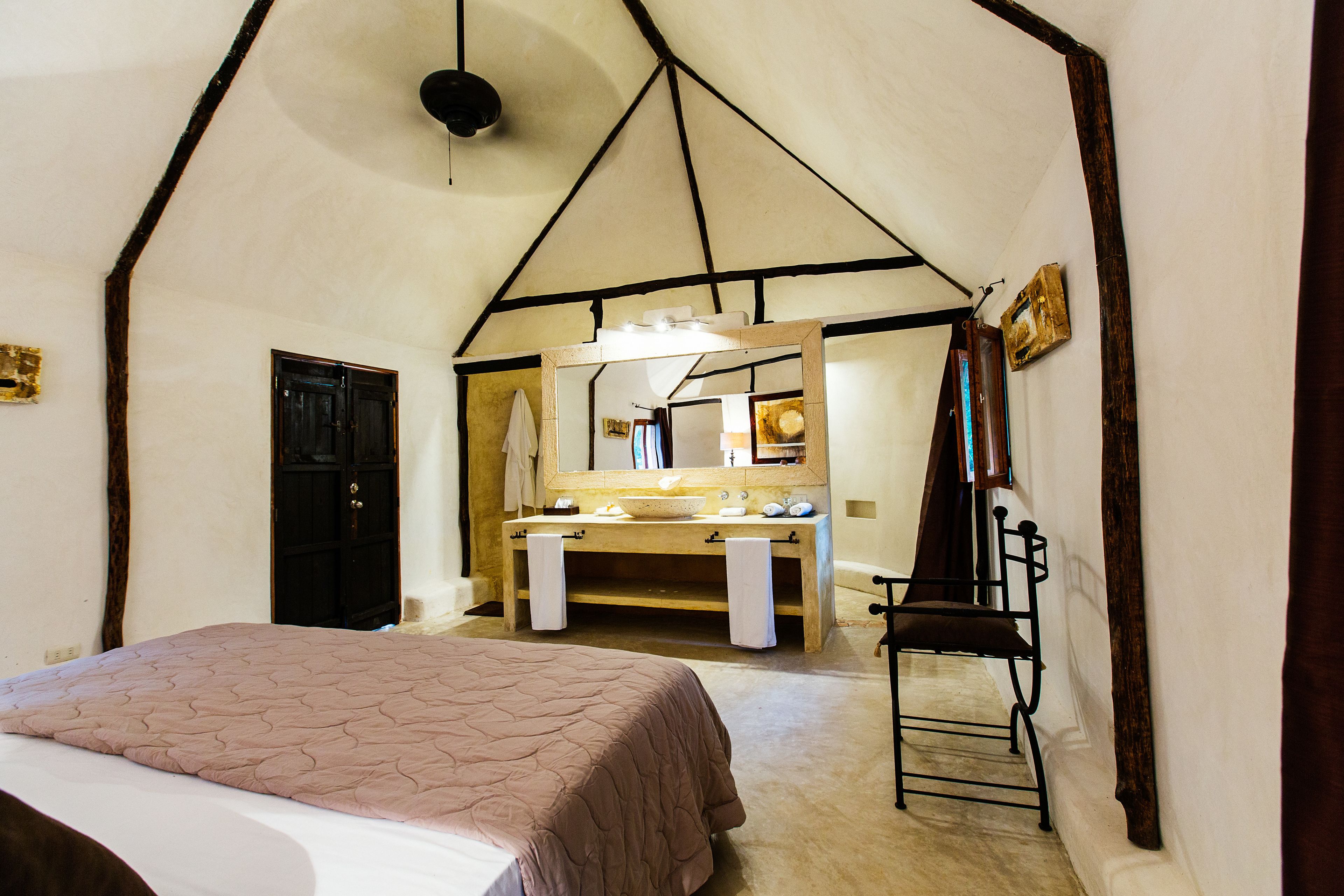 Un dormitorio con cama, banca de madera, lavamanos y espejo.