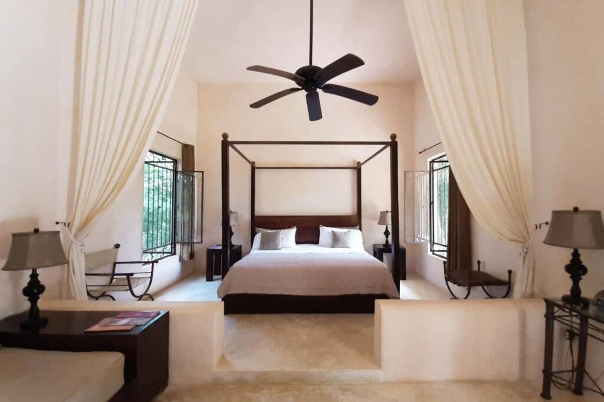 A four-poster bed with a ceiling fan, bedside tables with lamps, and curtains on either side.