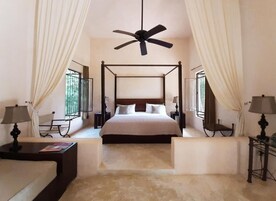 A four-poster bed with a ceiling fan, bedside tables with lamps, and curtains on either side.