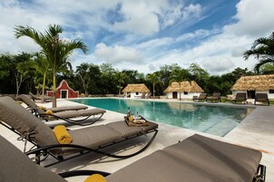 A poolside area with lounge chairs, a thatched-roof building, and a palm tree.