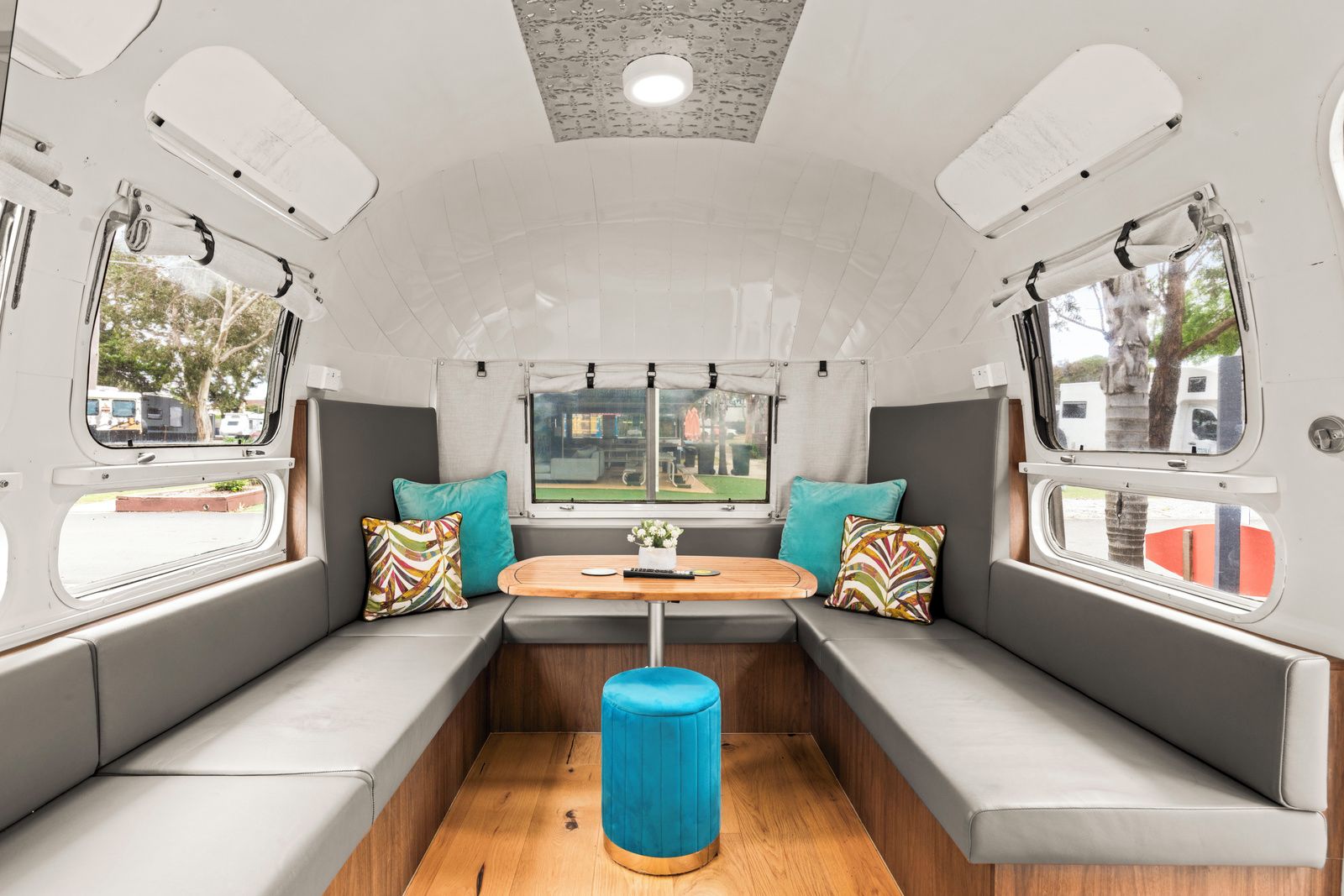 An RV interior with a central seating area, a table, and windows.