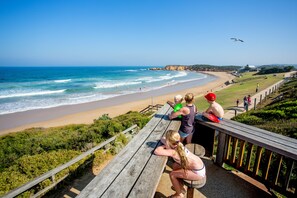A wooden bench overlooking a beach with waves, a clear sky, and a distant cliff. - Ingenia Holidays Torquay (Torquay)