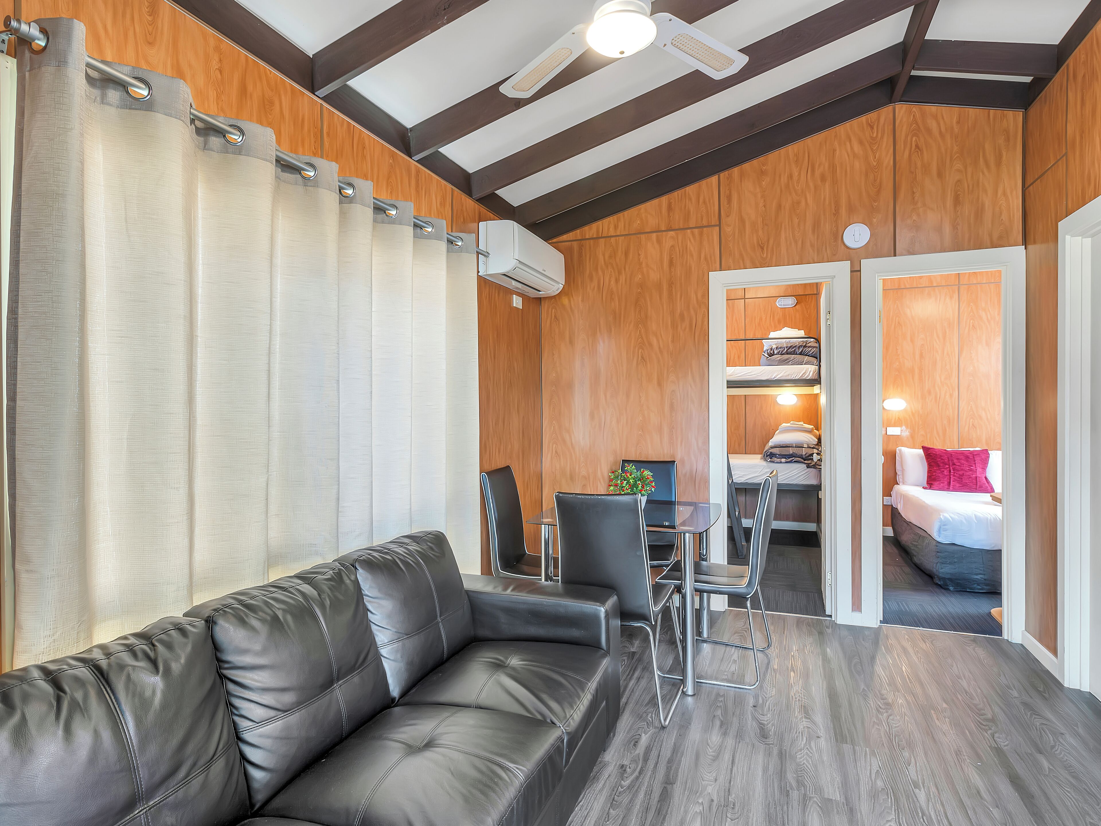 A modern room with a leather sofa, a dining table with chairs, and a bunk bed with a red pillow.