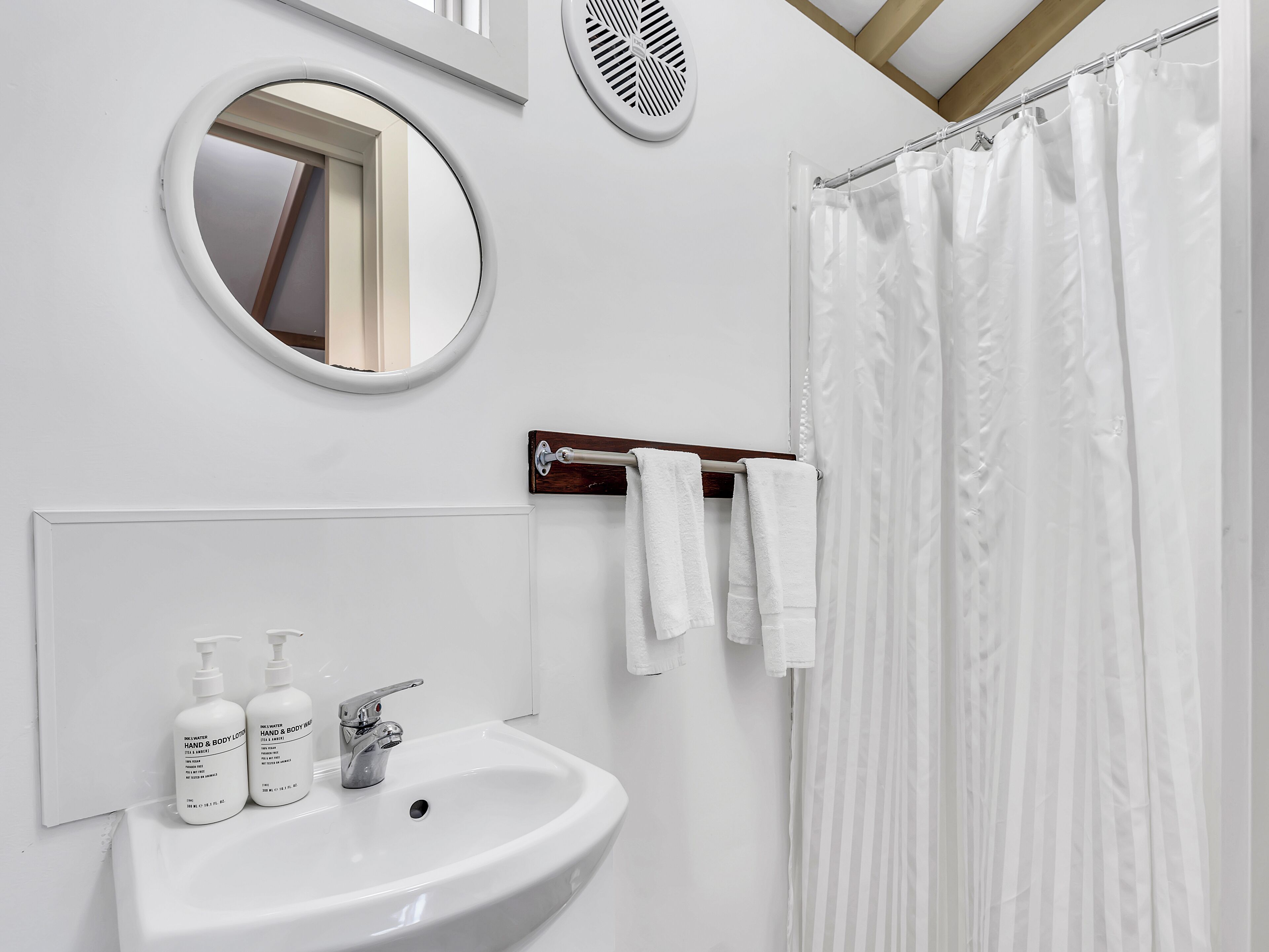 Ein Badezimmer mit einem weißen Waschbecken, zwei Flaschen Hand- und Körperlotion, einem Spiegel und einer Duschvorhang.