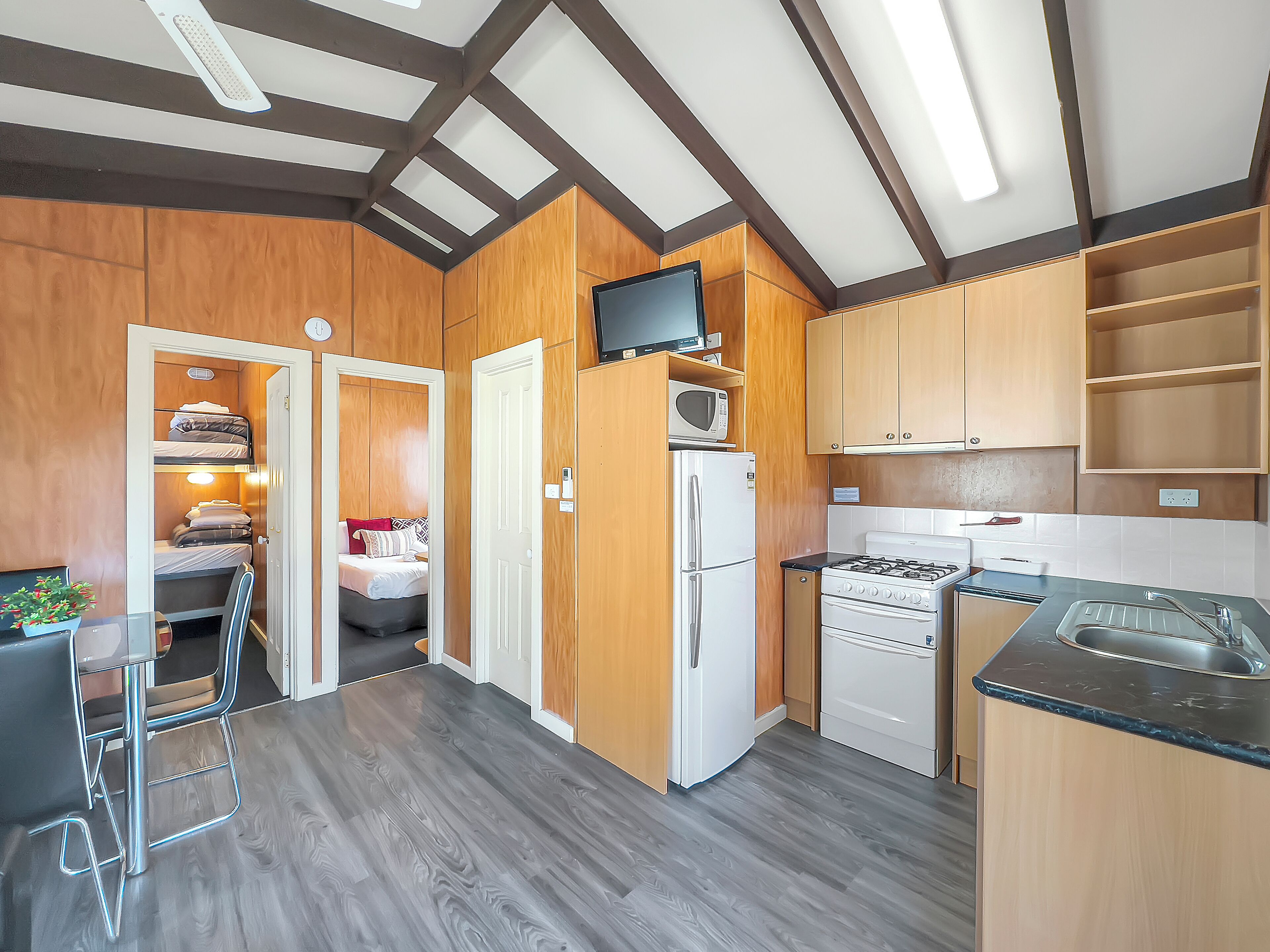 A compact kitchen with wooden cabinets, a refrigerator, a microwave, a stove, and a sink.