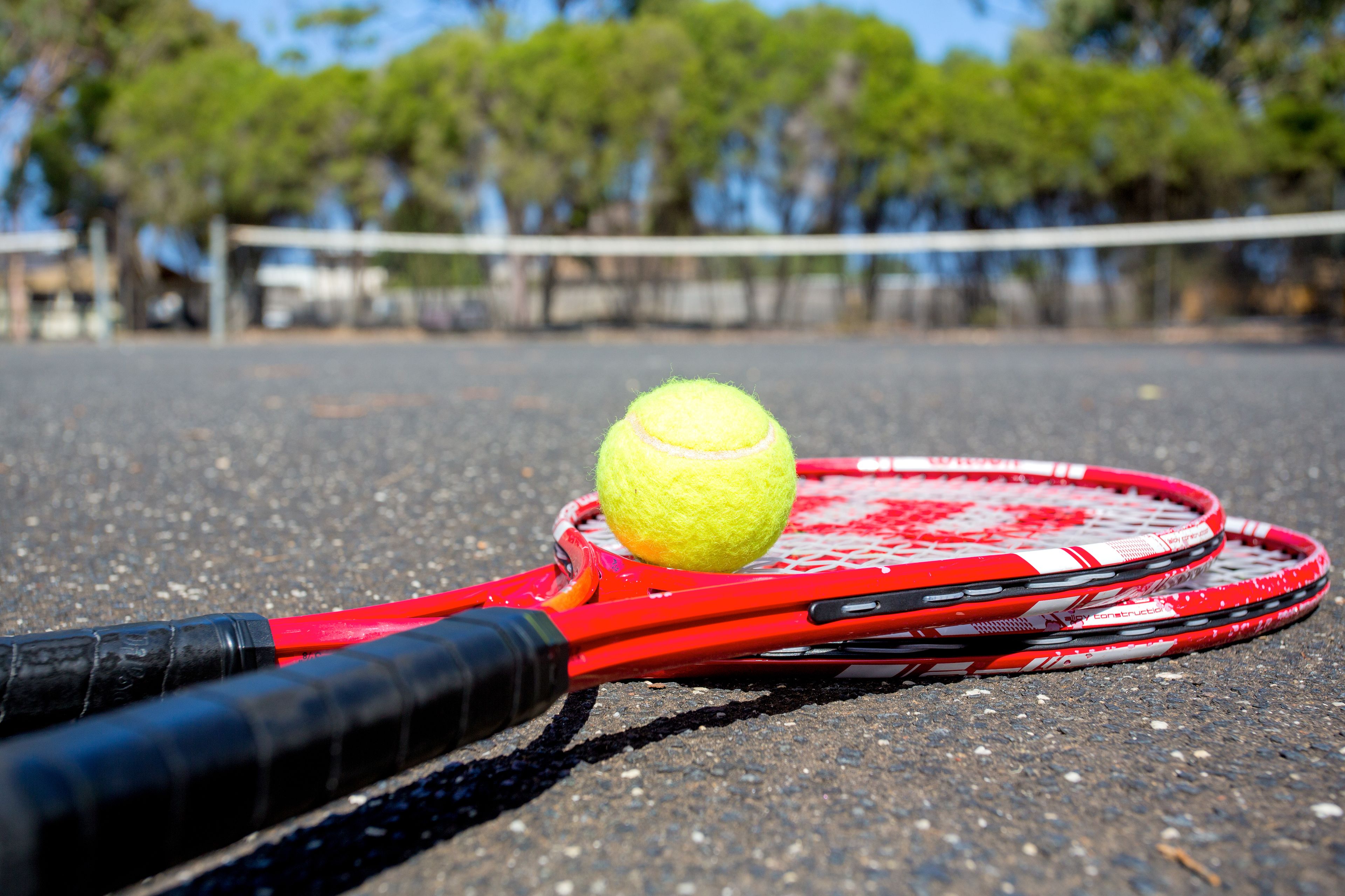 A tennis ball on a red and black tennis racket on a court.