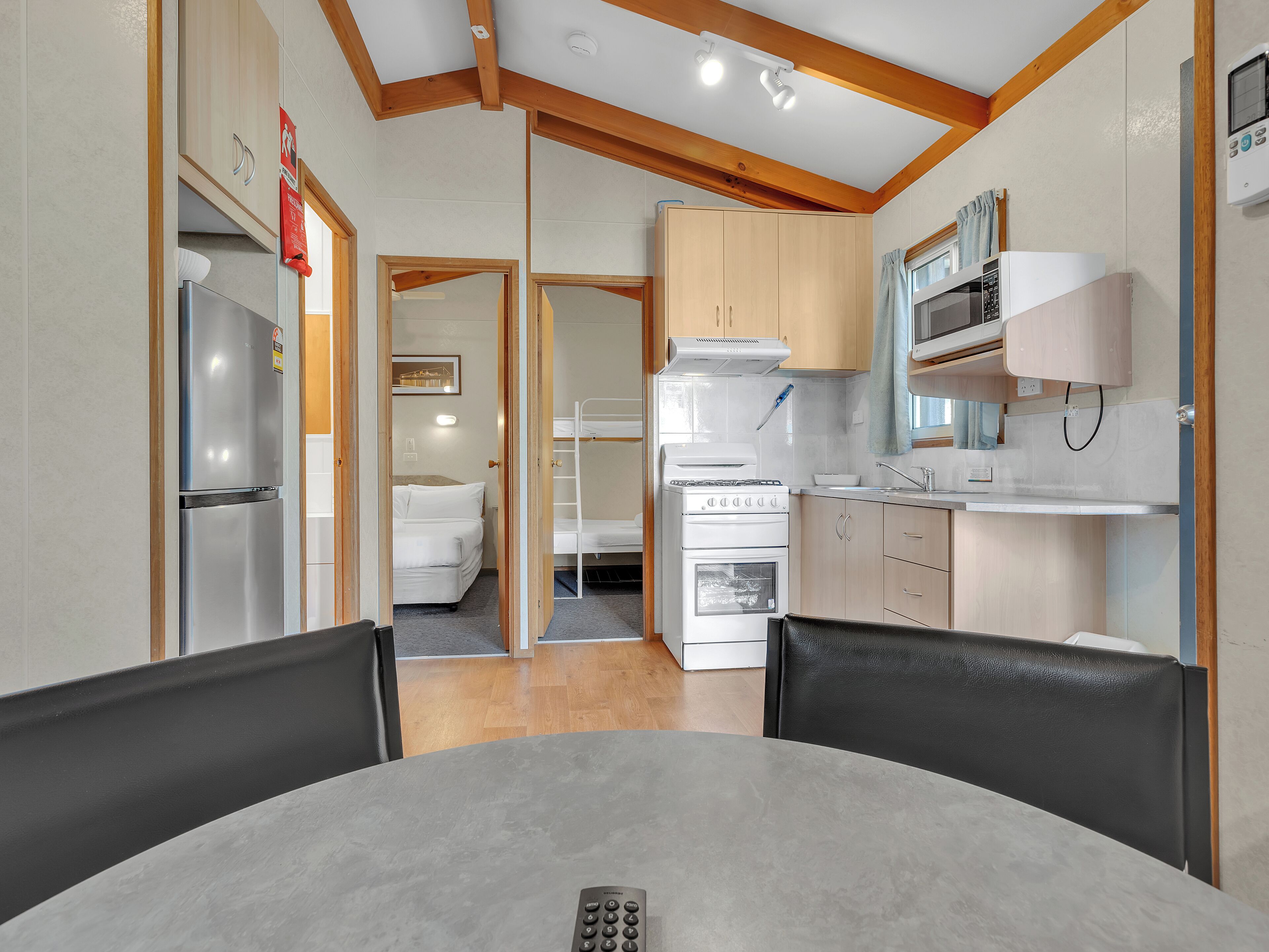 A compact kitchen with a refrigerator, stove, microwave, and sink. There is a dining table with chairs in the foreground.