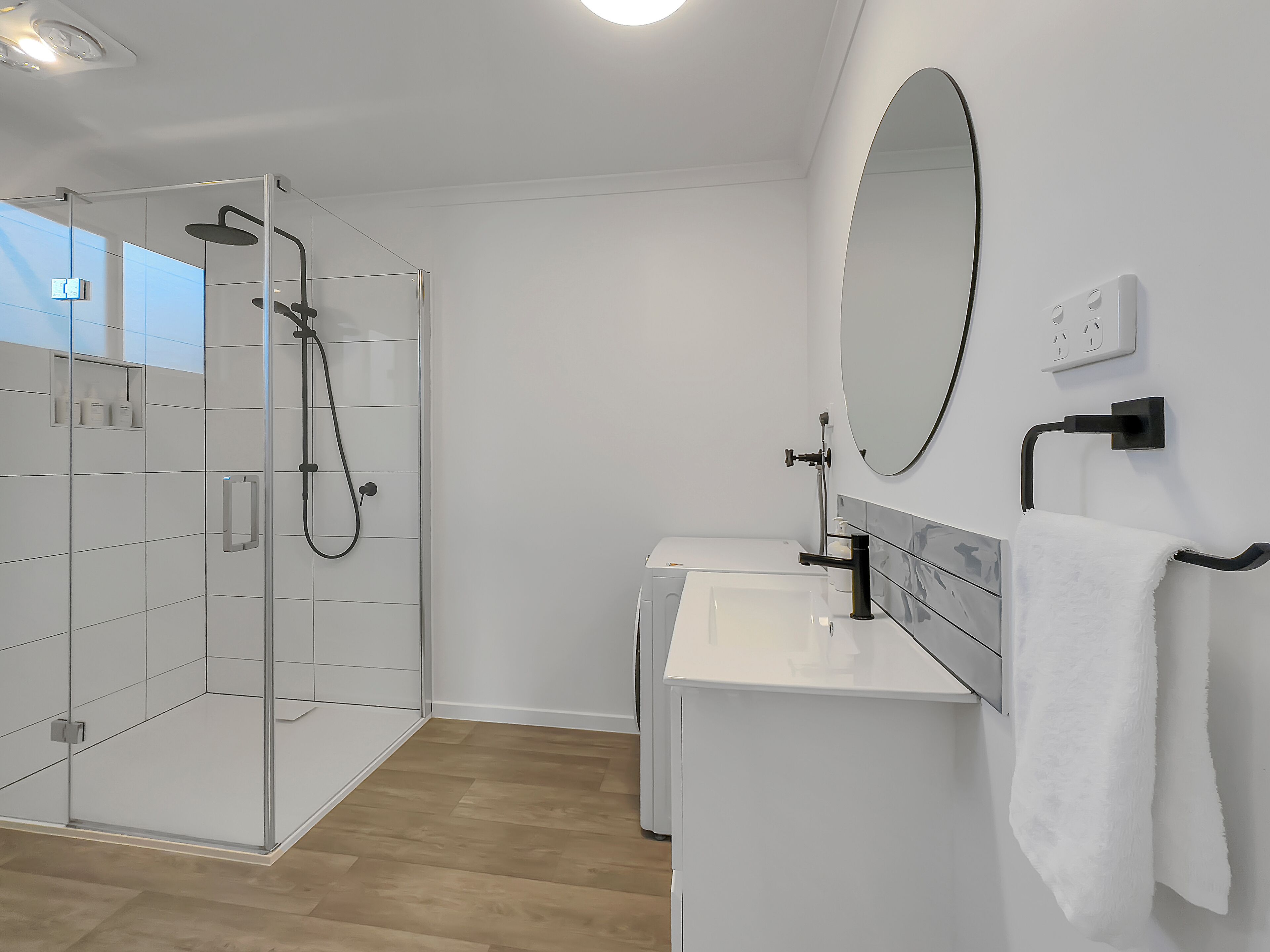 A modern bathroom with a glass-enclosed shower, a white sink, and a mirror.