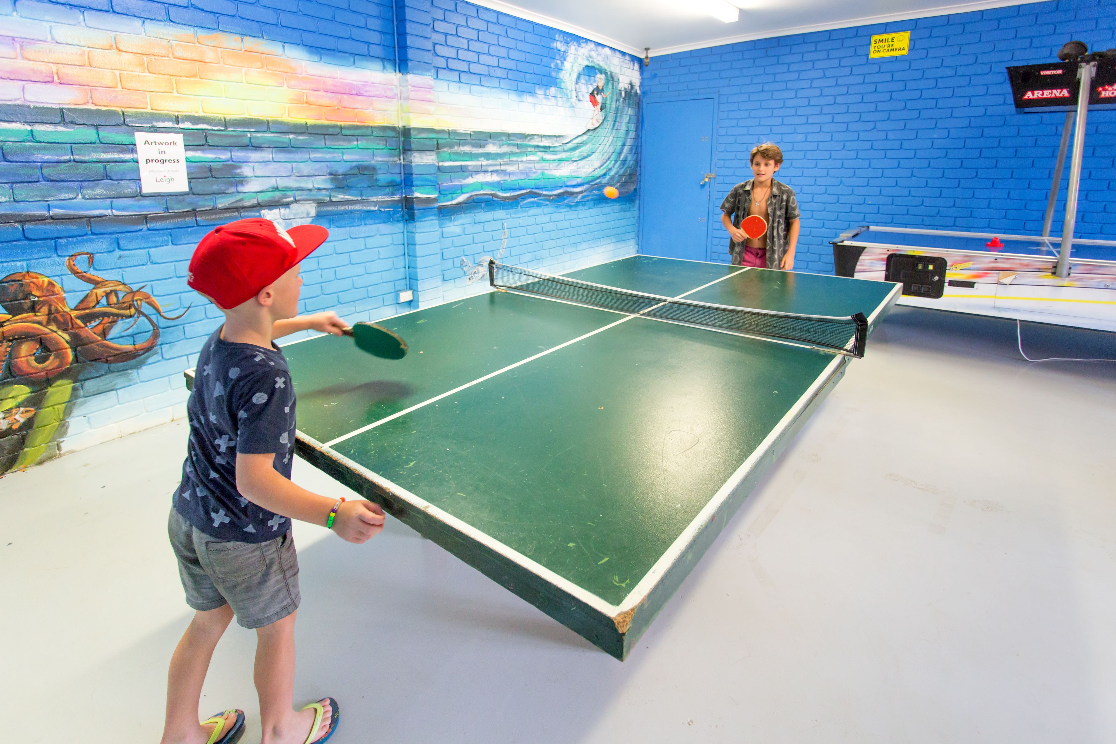 A ping pong table in a room with blue brick walls and a mural of a wave.