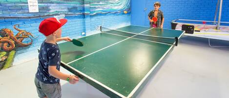 A ping pong table in a room with blue brick walls and a mural of a wave.
