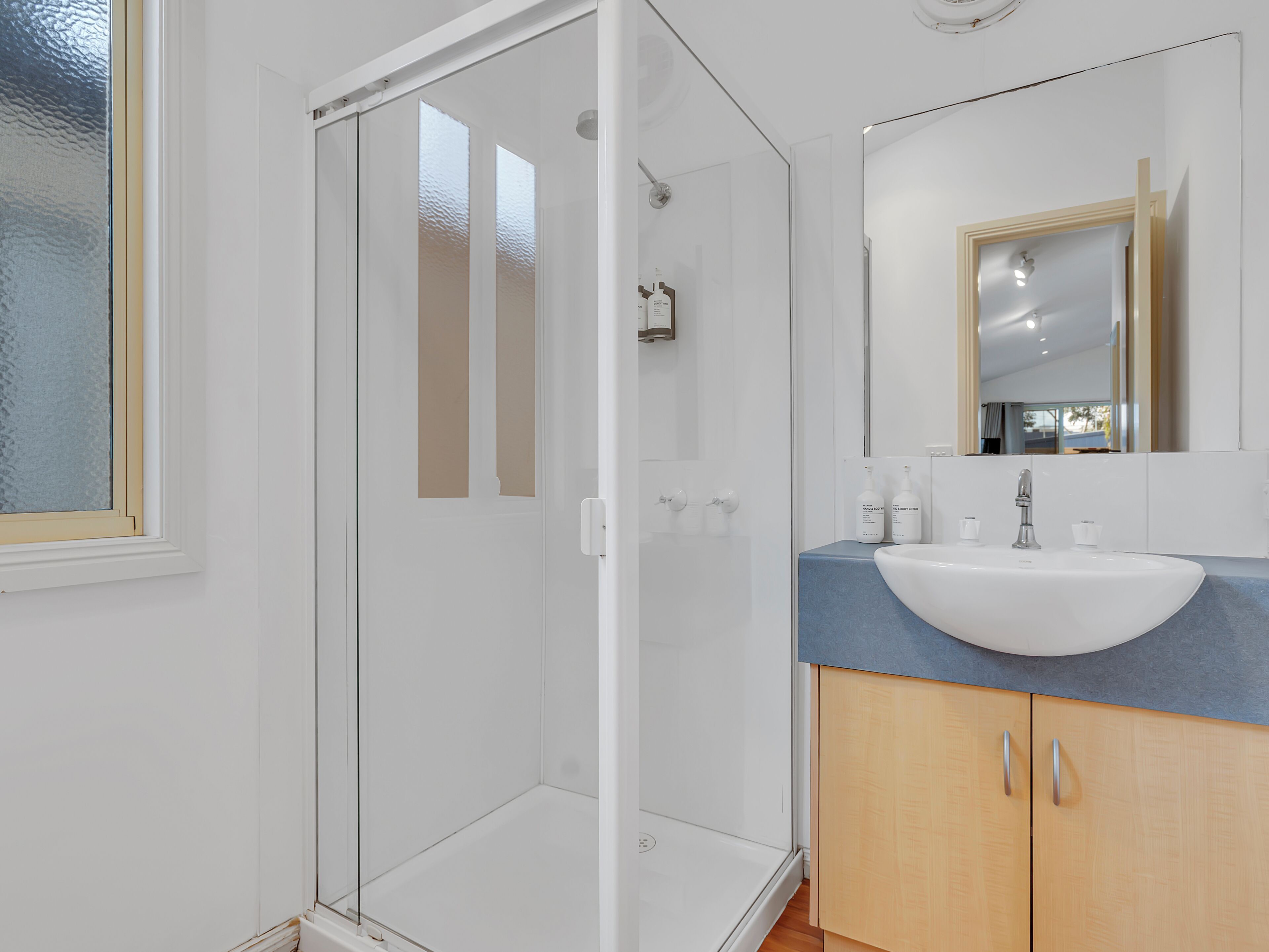 A modern bathroom with a glass shower enclosure, a white sink, and wooden cabinets.