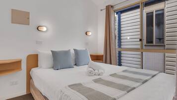 A neatly made bed with a patterned throw, a bedside table, and a wall-mounted light fixture.