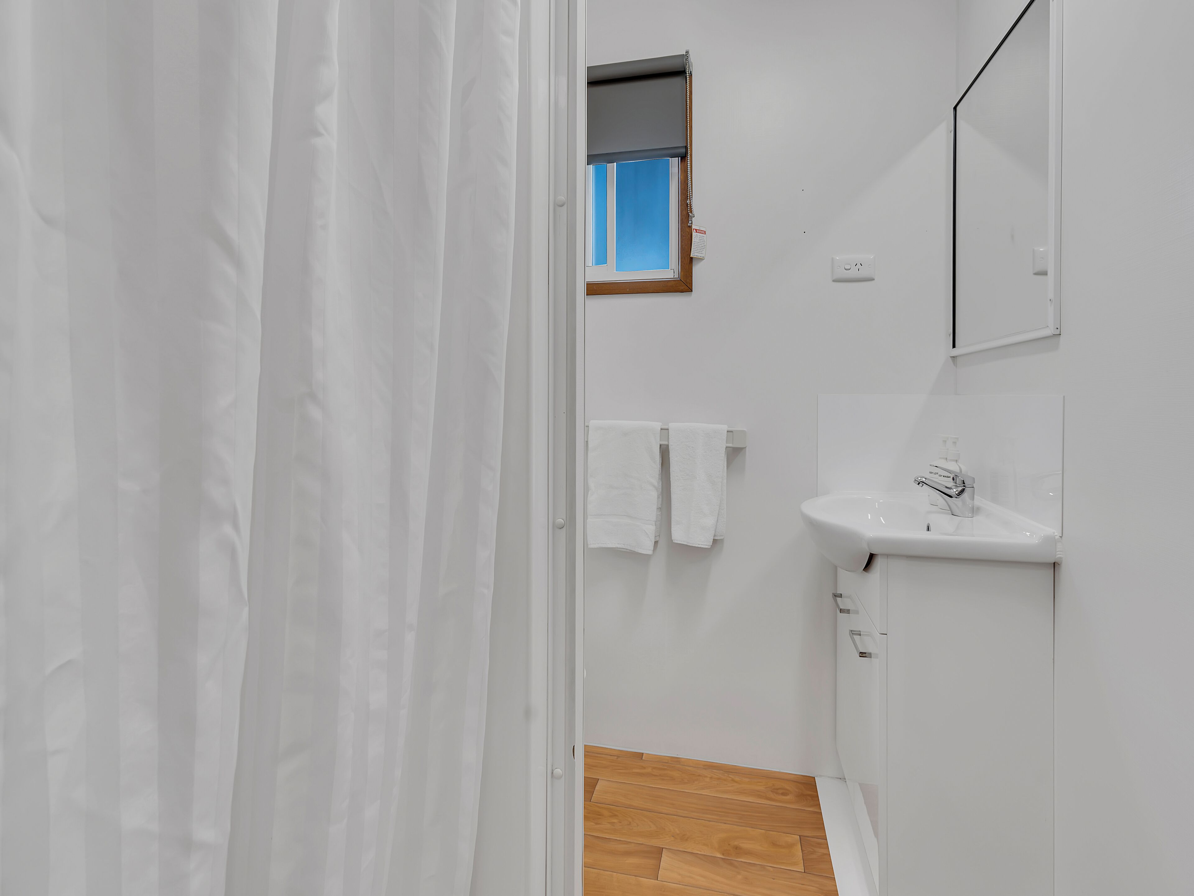 A bathroom with a white sink, a mirror, and a window with a blue view.
