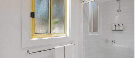 A bathroom with a glass shower enclosure, a toilet, and a window with a yellow frame.