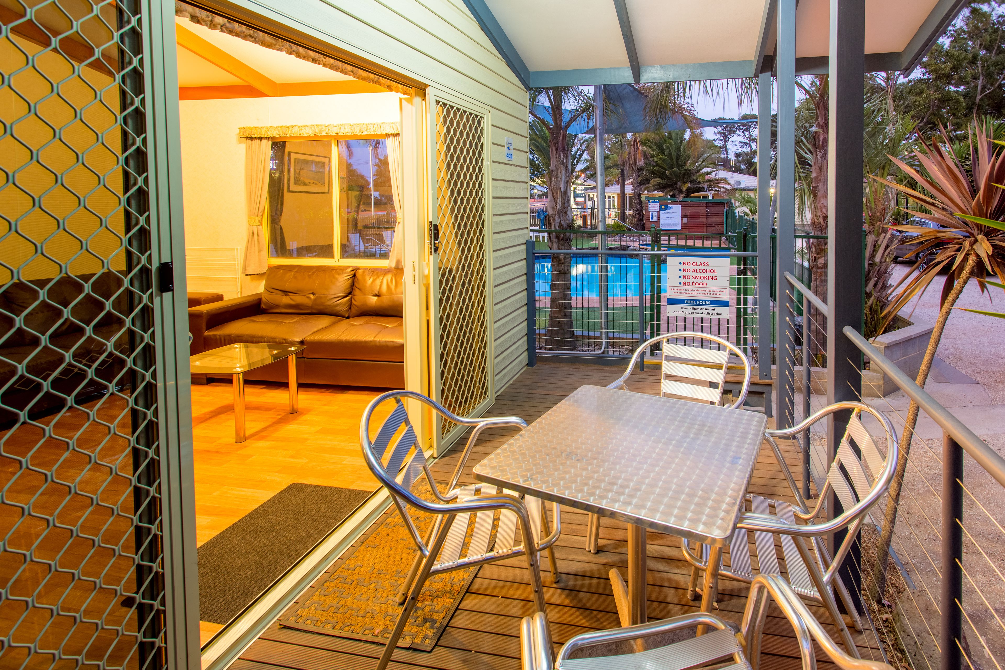 An outdoor patio with a table and chairs, a cushioned seating area, and a view of a swimming pool.