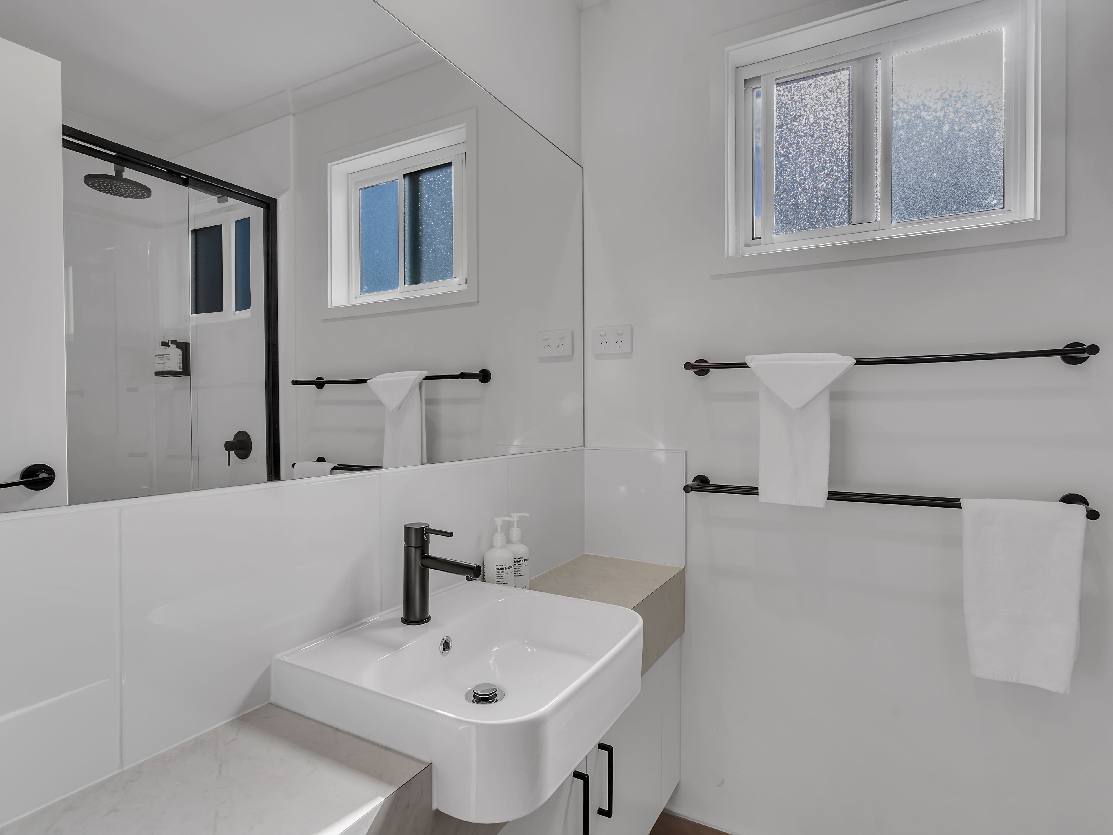 Een moderne badkamer met een witte wastafel, een spiegel en een raam.