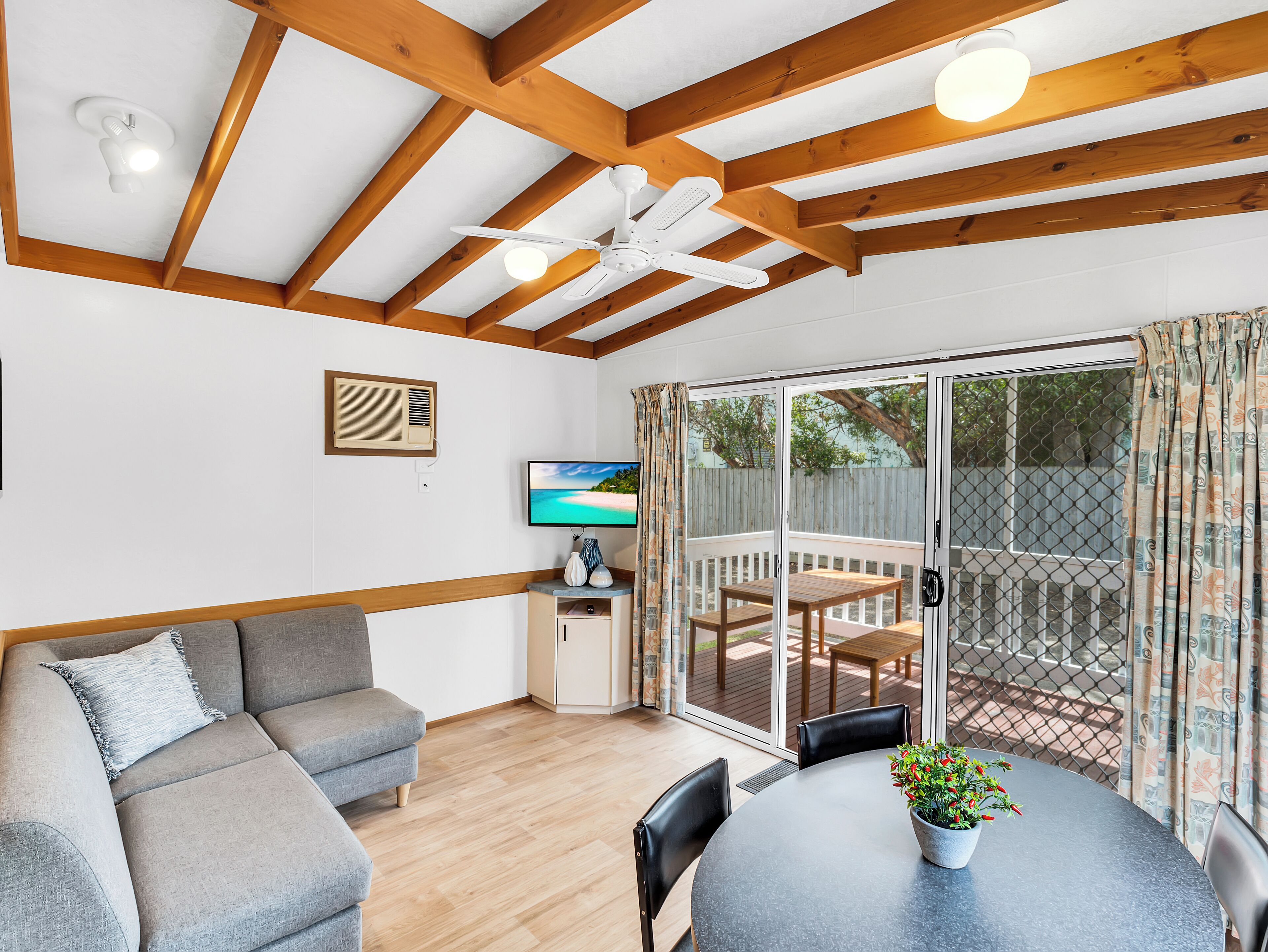 Une pièce chaleureuse avec un plafond en bois, un canapé, une table avec des chaises et un téléviseur fixé au mur.