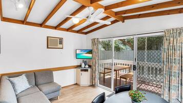 Une pièce chaleureuse avec un plafond en bois, un canapé, une table avec des chaises et un téléviseur fixé au mur.