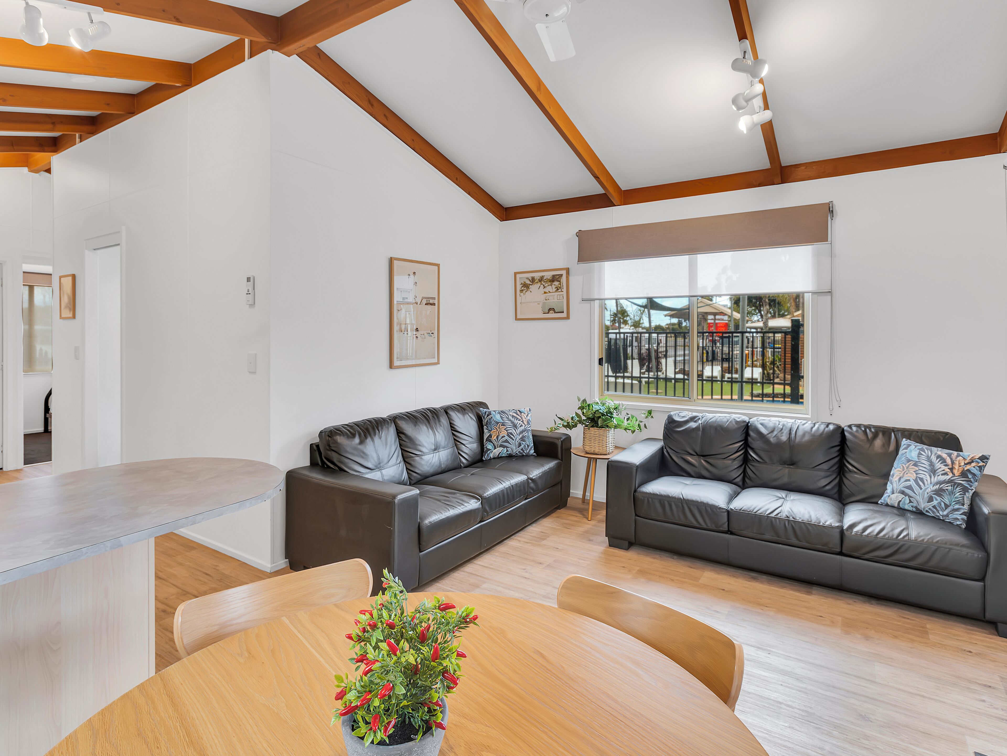 A modern living room with a wooden dining table, two leather sofas, and a large window with a view of the outside.
