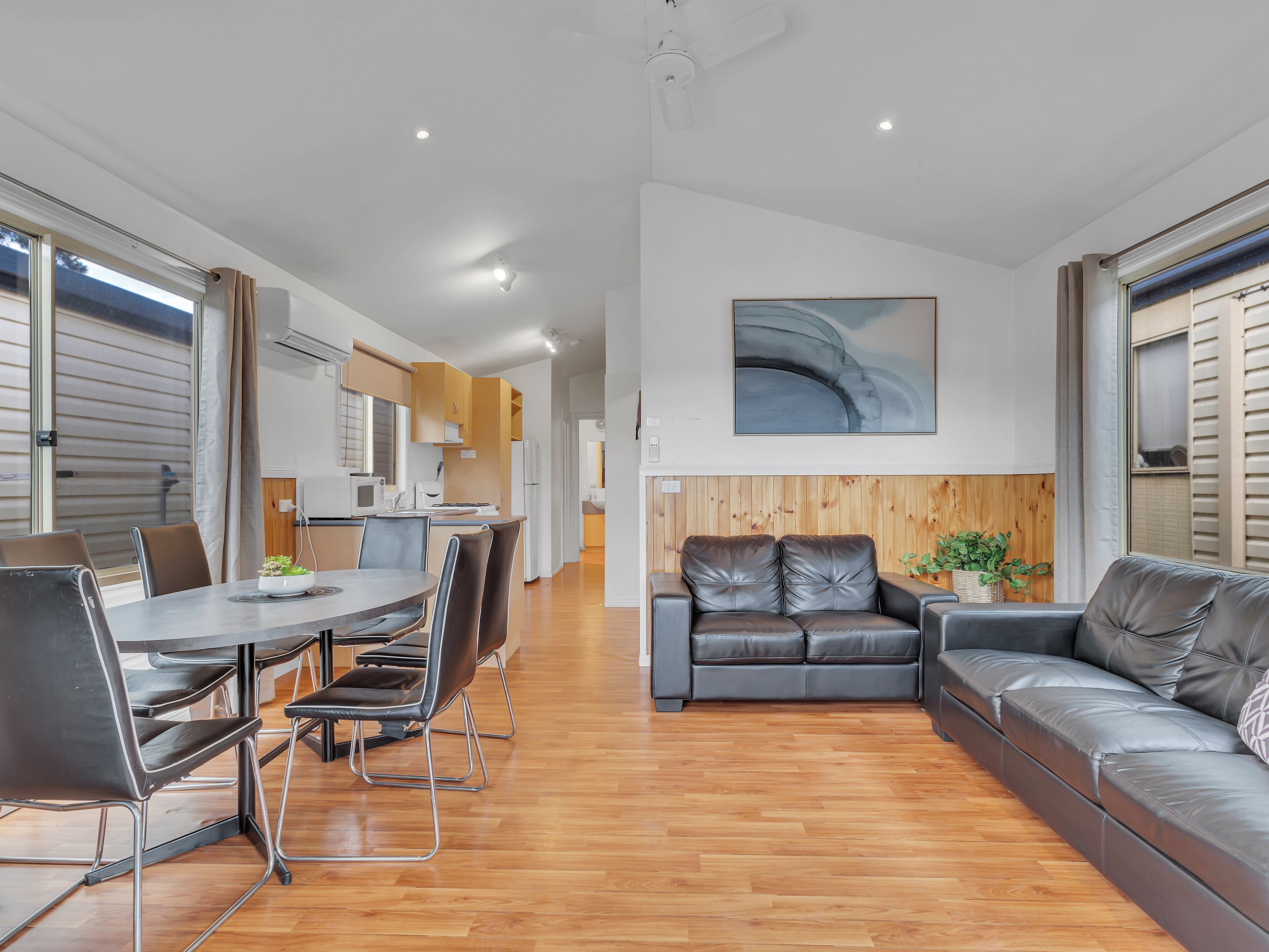 A modern living room with a dining area, wooden flooring, and a large window with blinds.