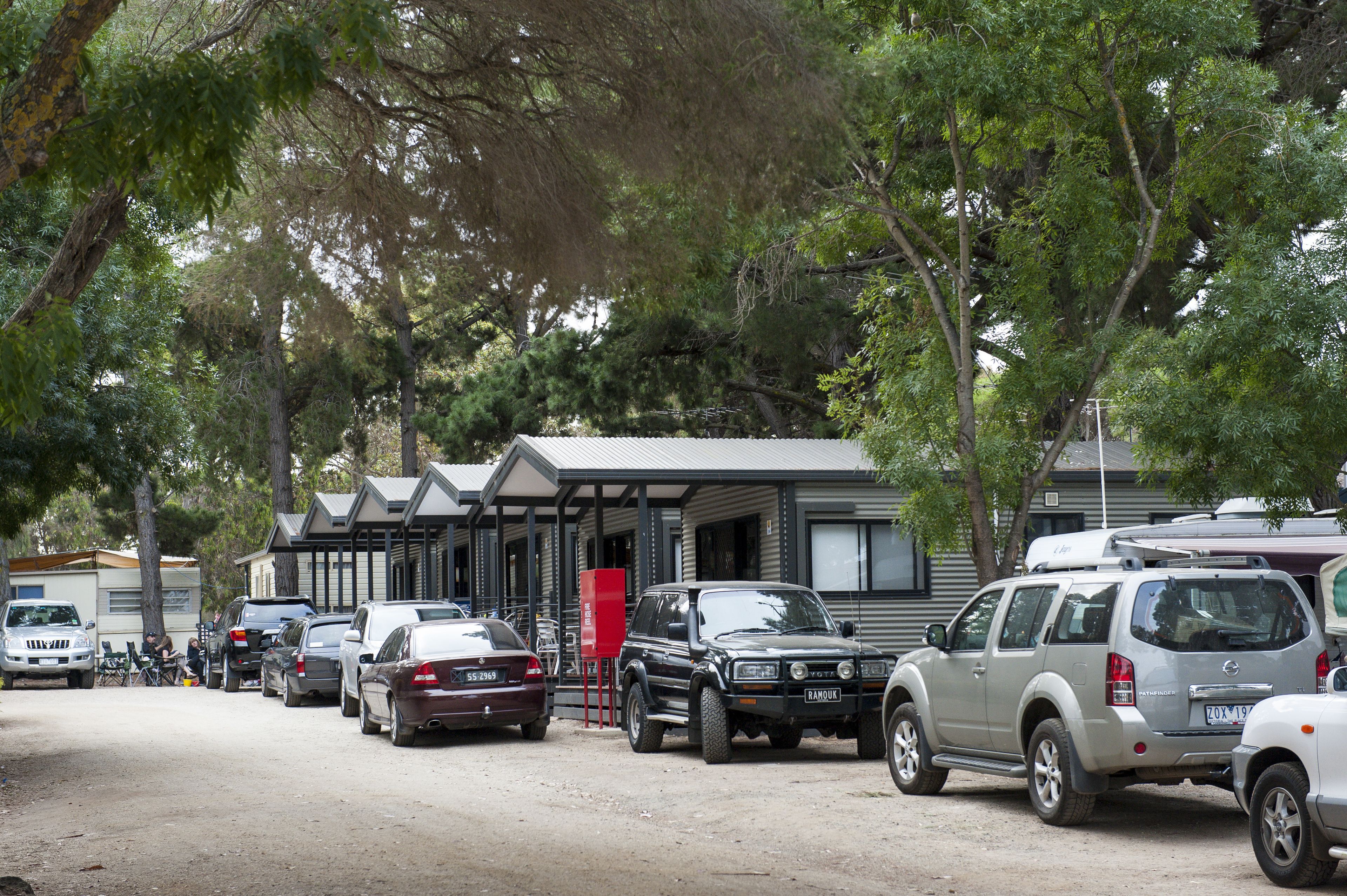 Una hilera de vehículos recreativos estacionados frente a una fila de casas móviles, con suelo de tierra.