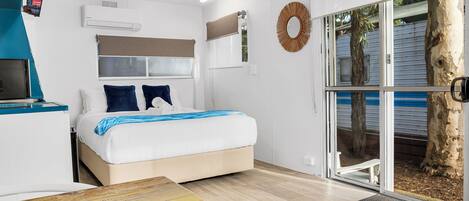 A modern bedroom with a bed, a desk, and a large window.
