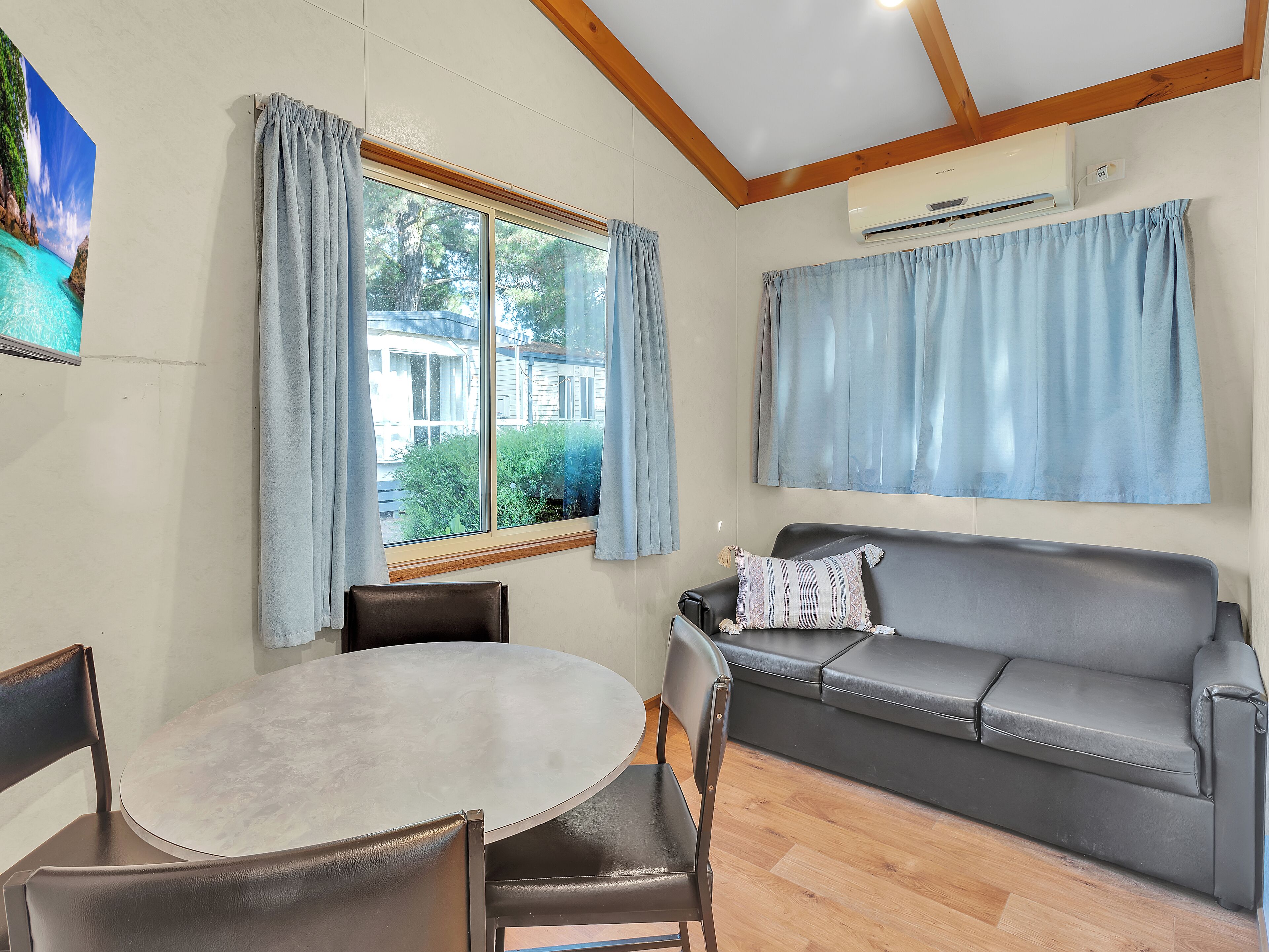 Una habitación con una mesa redonda, dos sillas, un sofá gris y una ventana con cortinas.