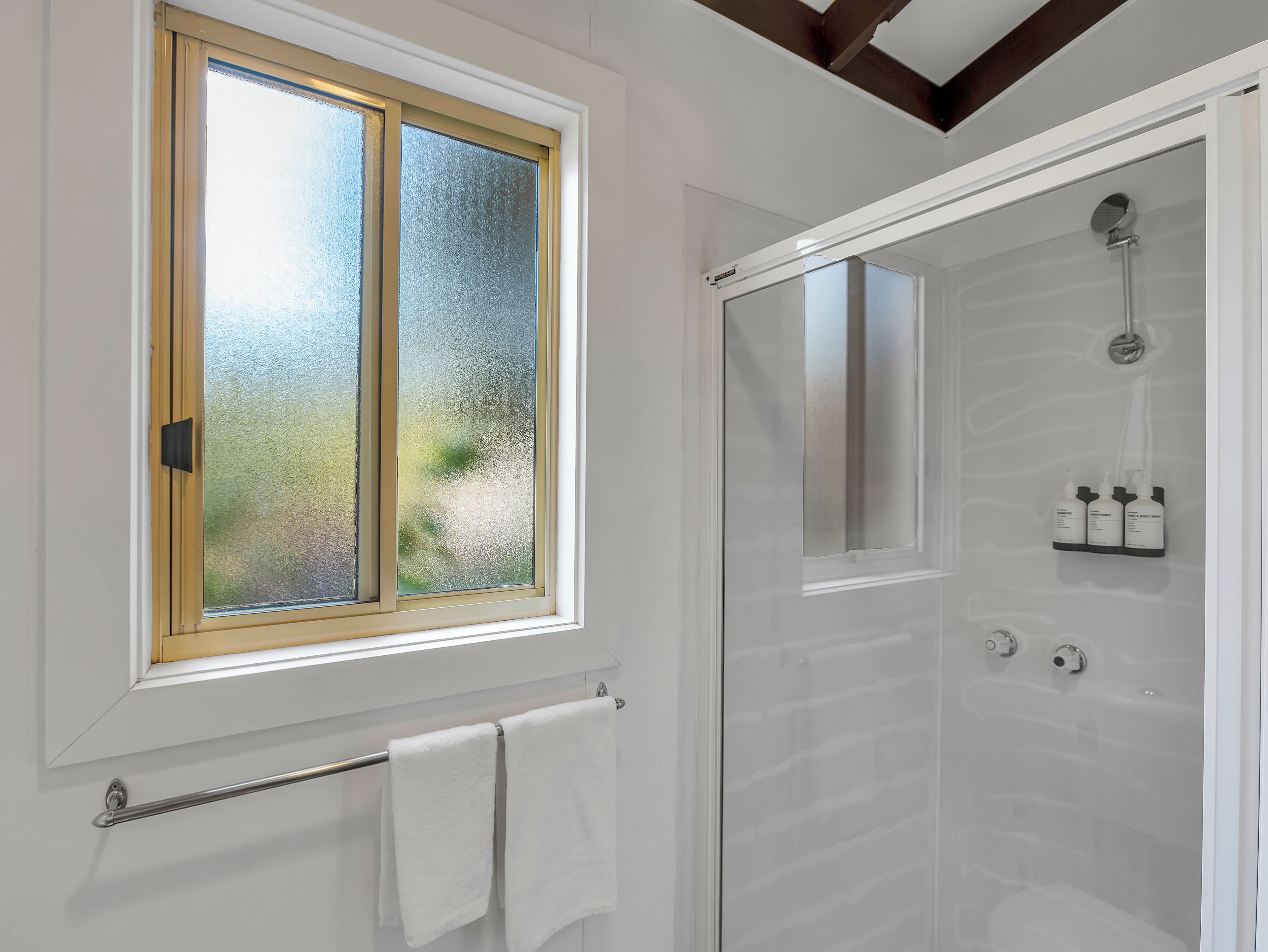 A bathroom with a frosted glass window, a shower with a glass door, and a towel rack with two towels.