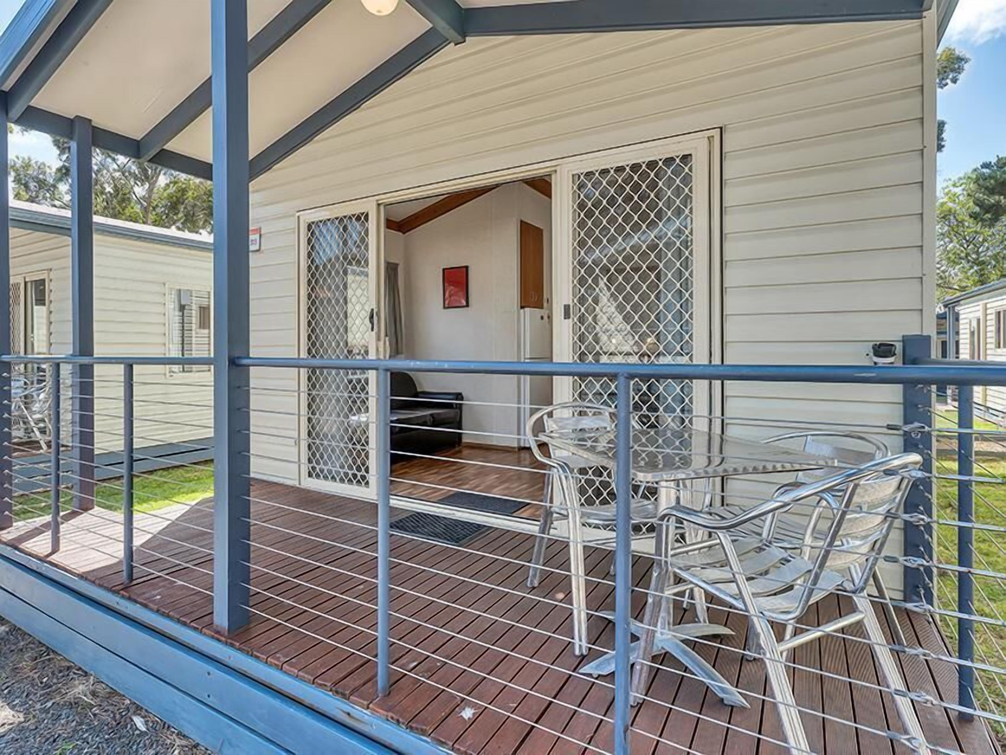 A covered outdoor area with a table and chairs, a wooden deck, and a building with a sliding glass door.