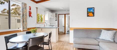 A modern kitchen with white cabinets, a dining table with chairs, and a grey sofa.