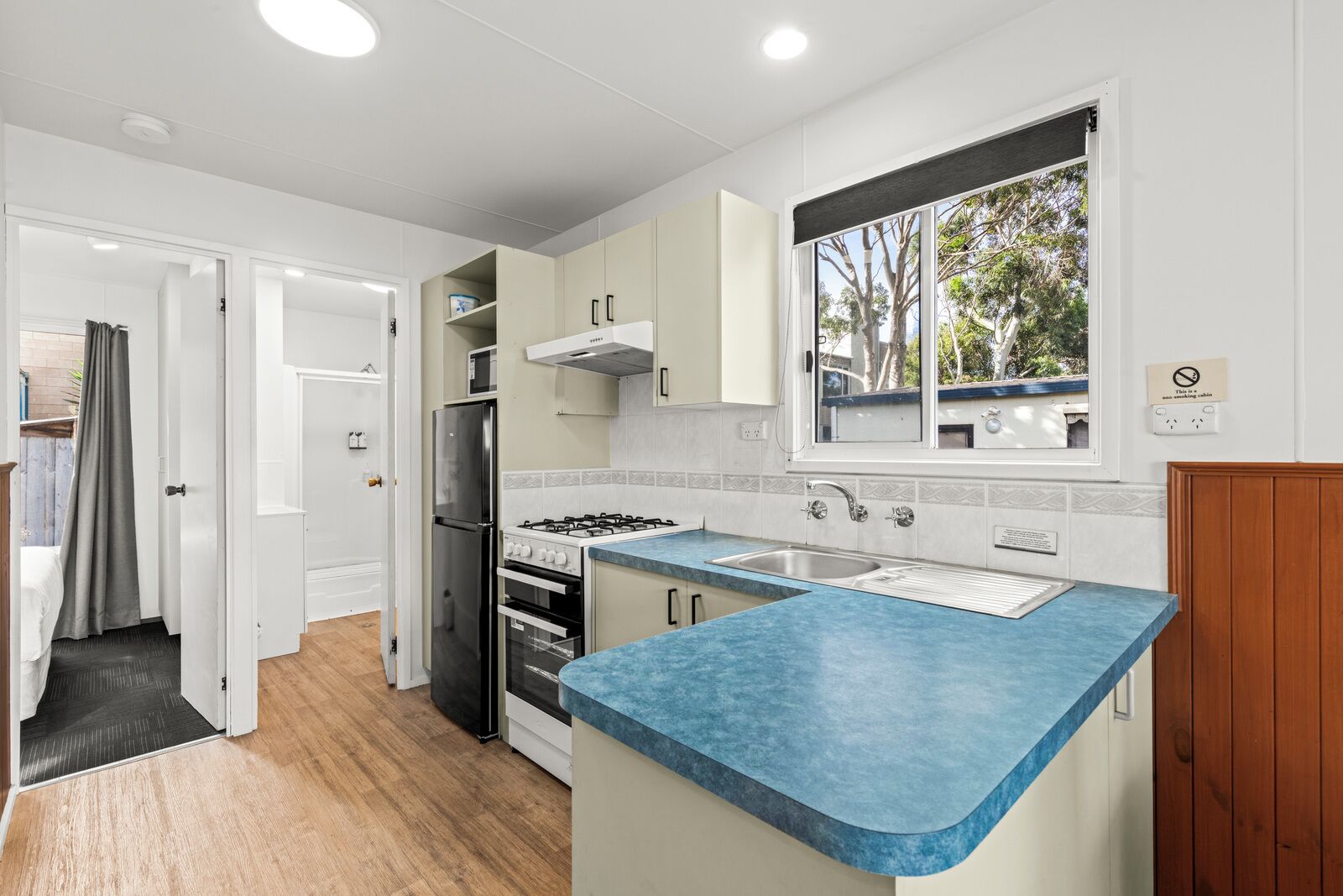 A compact kitchen with a blue countertop, white cabinets, a stainless steel refrigerator, and a gas stove.