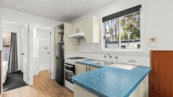A compact kitchen with a blue countertop, white cabinets, a stainless steel refrigerator, and a gas stove.