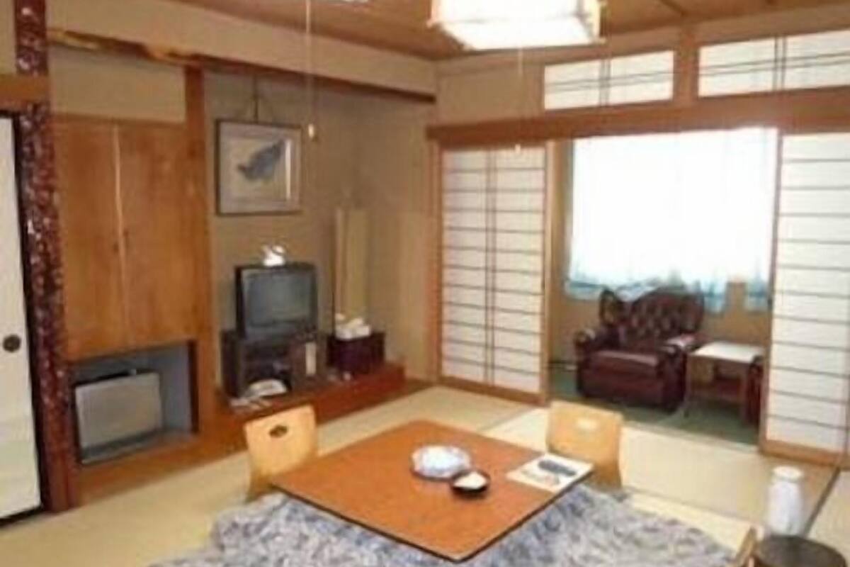A traditional Japanese-style room with tatami flooring, a low table with a cushion, a television, and sliding doors.