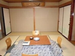 A traditional Japanese-style room with tatami flooring, a low table with a cushion, and sliding doors. - Daimaruya Ryokan (Yamanouchi)