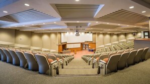 Uma sala de conferências com fileiras de cadeiras, um pódio e uma tela grande.