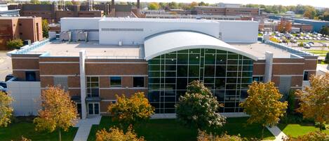 A modern building with a curved glass facade, surrounded by trees and a parking lot.
